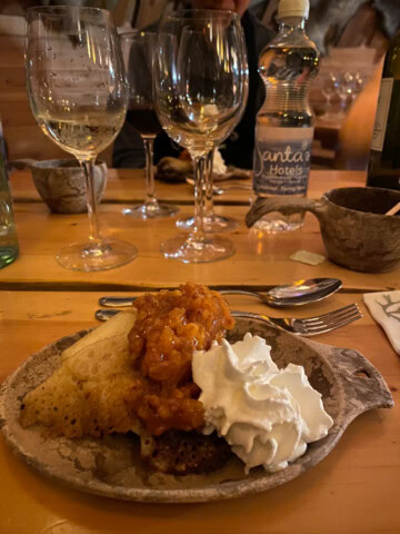 A dessert topped with whipped cream and fruit sauce on a plate, set on a wooden table with wine glasses and a water bottle in the background, evokes the cozy charm of Finland's rustic cafes.