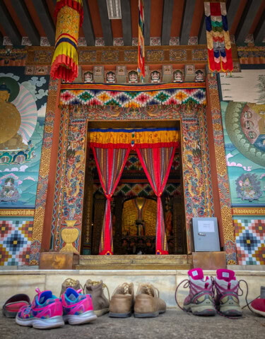 Colorful temple entrance with intricate artwork and curtains, typical of Bhutan’s rich heritage. Various shoes and sandals are left outside on the ground, a common sight for those exploring the enchanting corners of this popular travel destination.