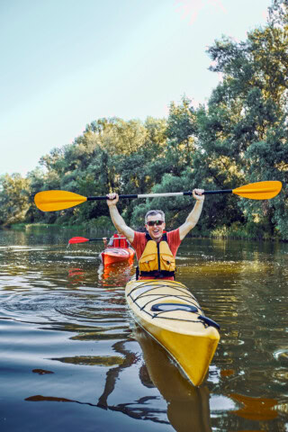 A person in a yellow kayak raises their paddle while another kayaker follows in a red kayak on a calm, tree-lined river, reminiscent of the tranquil waters of Palau.
