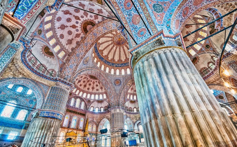 Intricately decorated columns and domes inside a mosque in Turkey, featuring detailed patterns and vibrant colors.