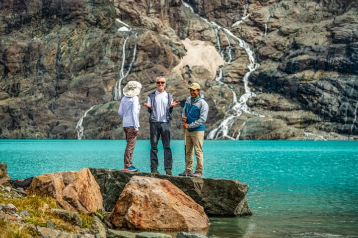 Three male hikers smiling and standing on a rock next to the glacial Laguna Azul in Estancia Helsingfors, Patagonia, Argentina