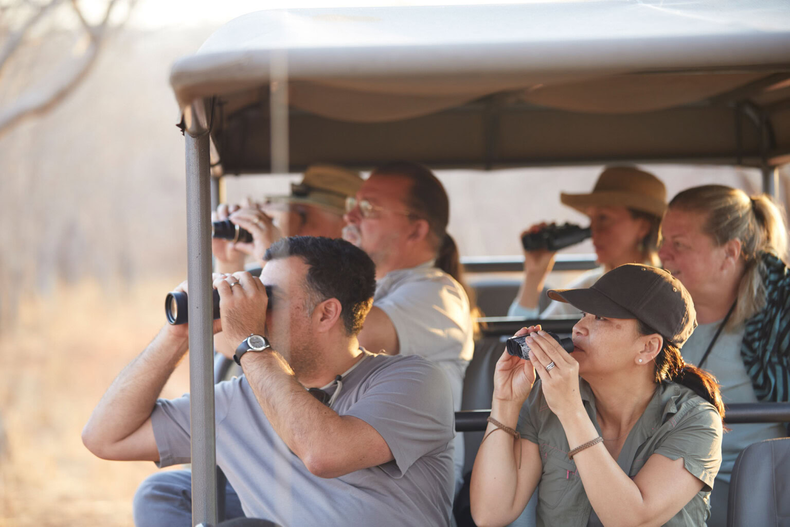 Group of travelers using binoculars from open-air jeep on safari in Zimbabwe.